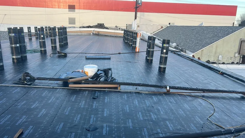 Rolls of Polyglass roofing material standing on a dark base sheet beside a roofing torch and hose