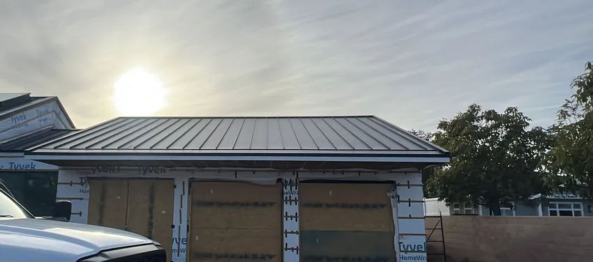Standing-seam metal roof on a garage still wrapped in white house wrap during renovation