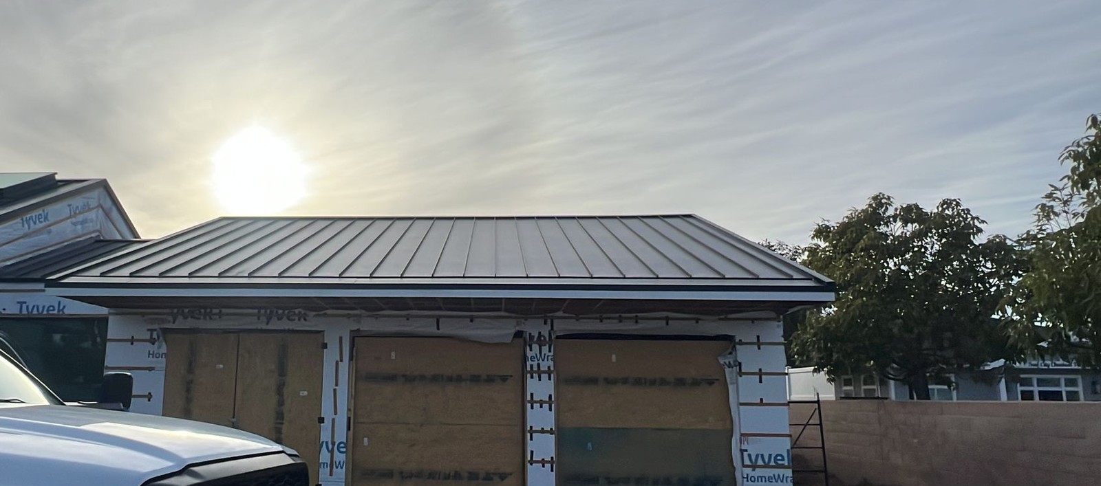 Dark standing-seam metal roof on a house under renovation, walls still covered in plastic house wrap