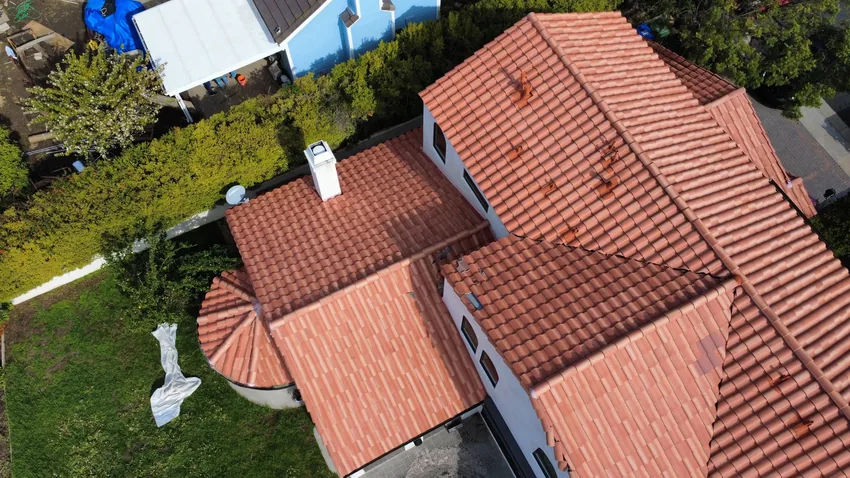Aerial view of a red clay tile roof with a rounded turret section and a white chimney