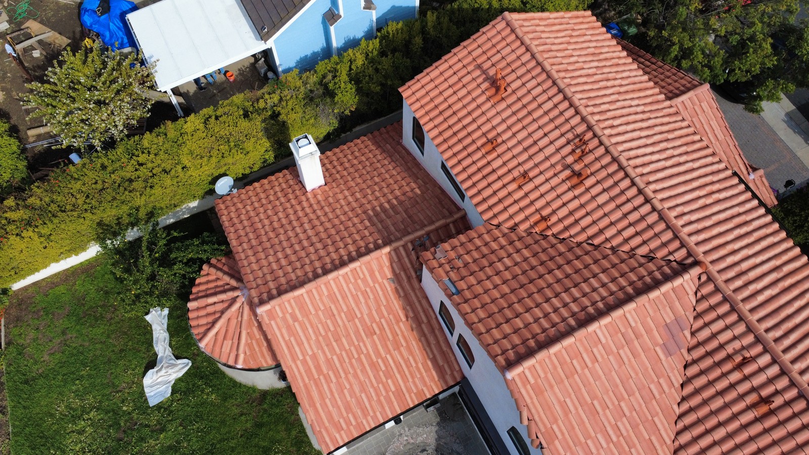 Aerial view of a red clay barrel tile roof with several gables, a chimney and a satellite dish.