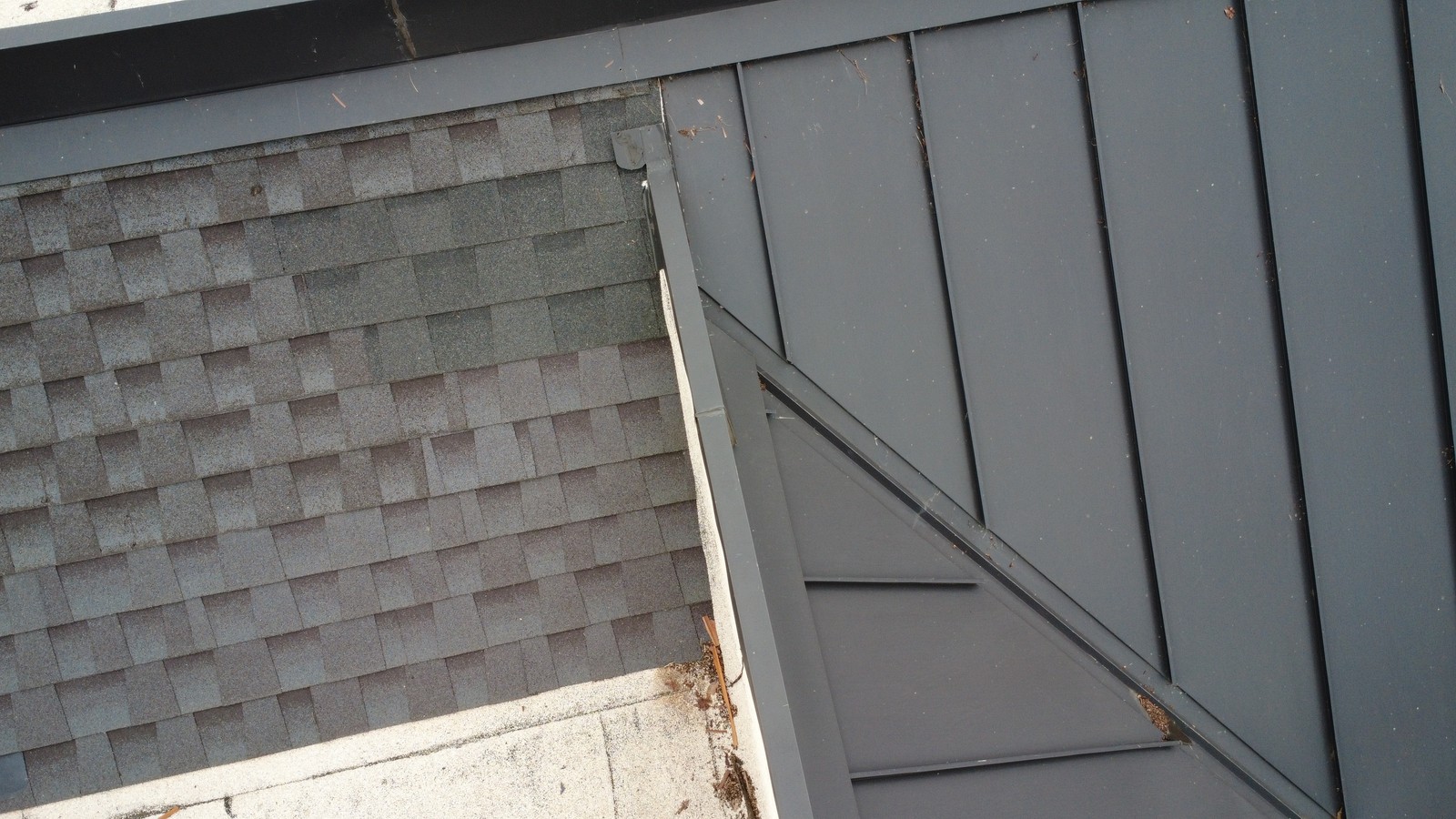 Gray asphalt shingles on one slope meeting dark gray standing-seam metal panels across a metal edge