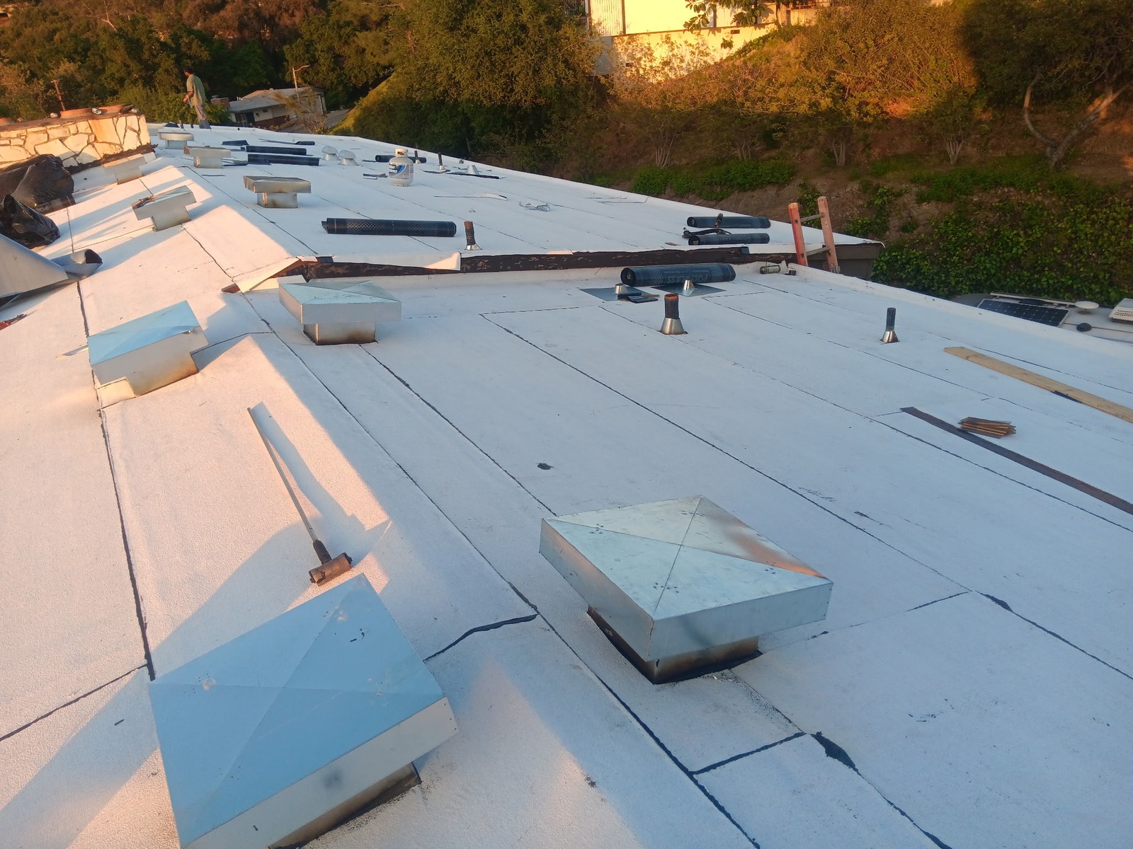 White-coated low-slope roof mid-job with metal vent hoods, pipe flashings and rolled roofing material
