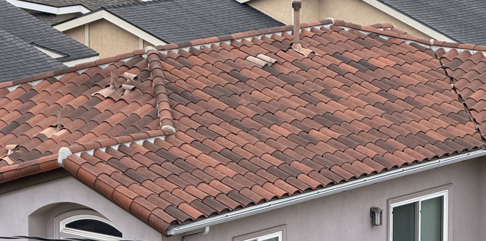 Close view of red clay tile roof planes with mortared hips, a metal flue pipe and a few loose tiles