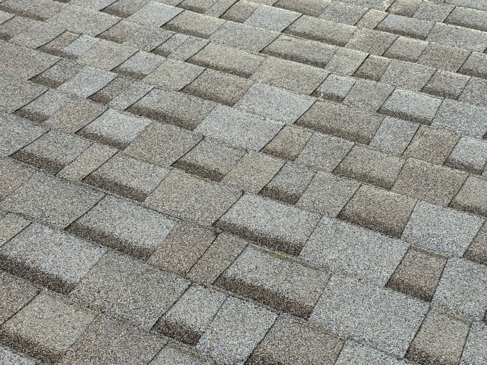 Close-up of weathered gray and brown asphalt shingle courses in a staggered pattern