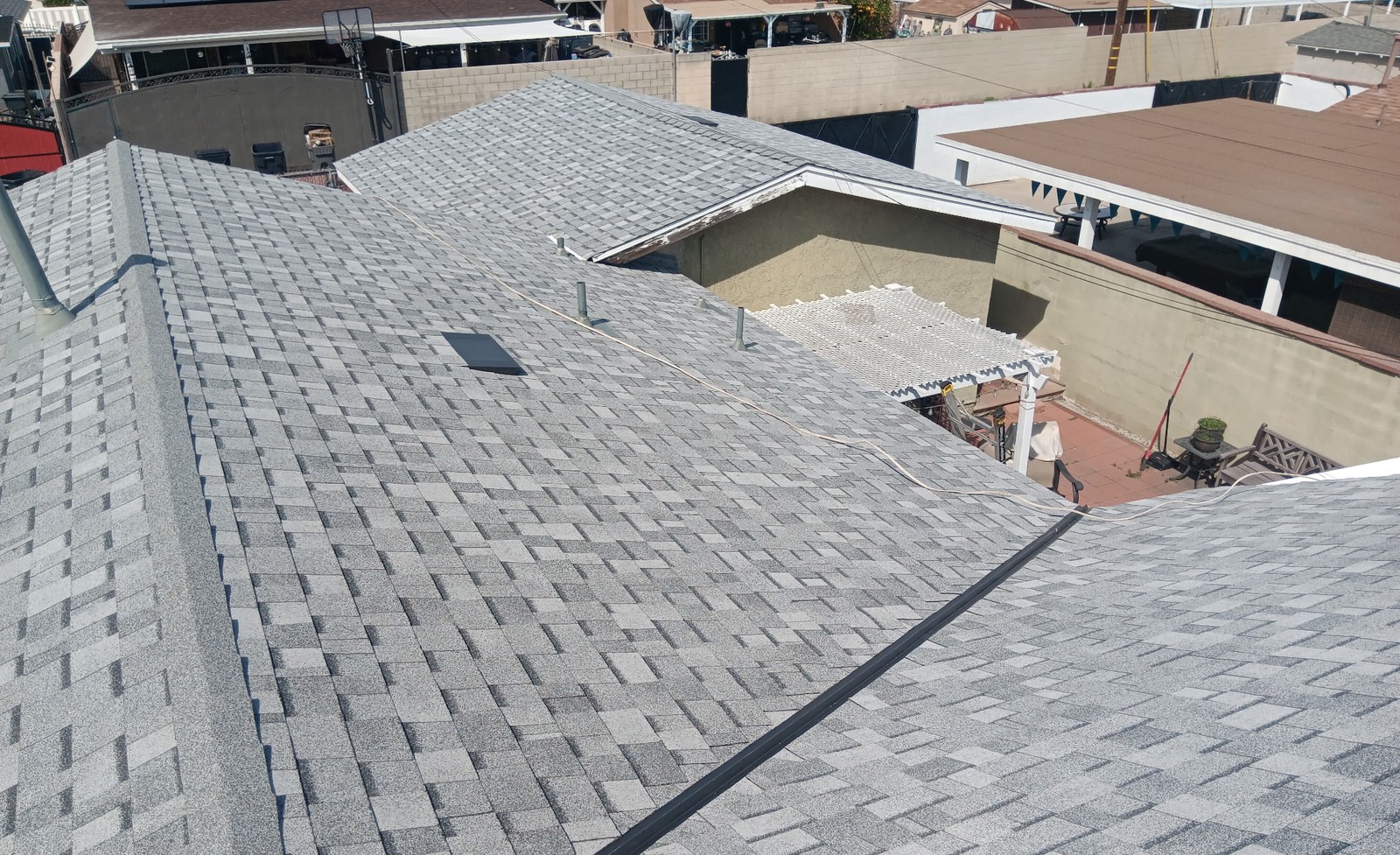 Aerial view of gray asphalt shingle roof slopes, ridges and a valley above a house and back patio
