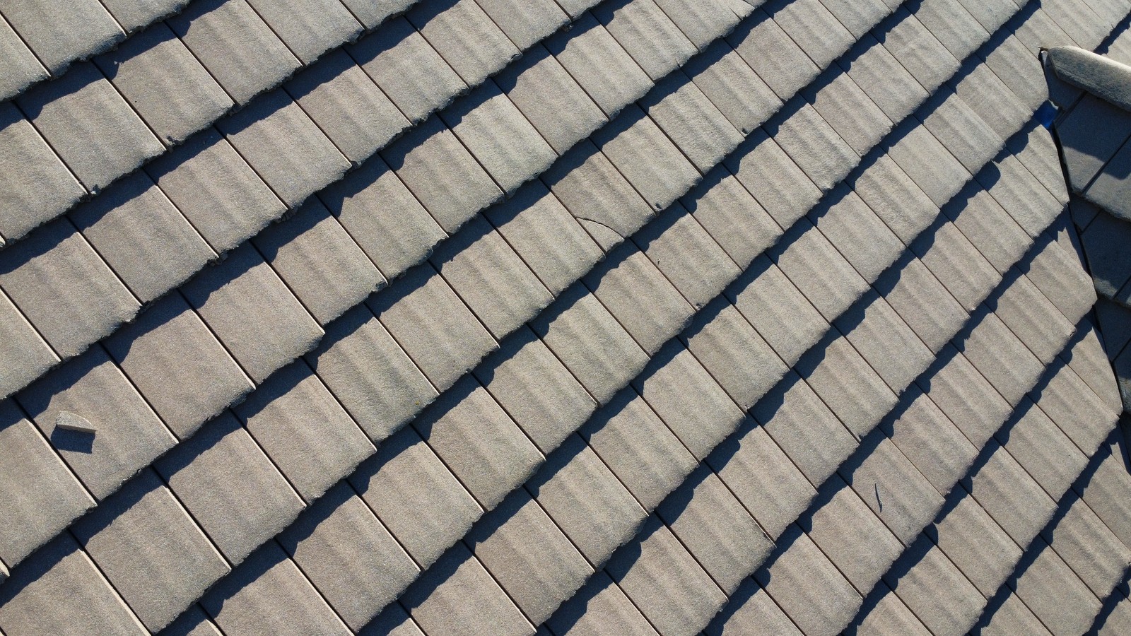 Close-up of gray flat roof tiles laid in rows, with a broken tile fragment lying on the surface