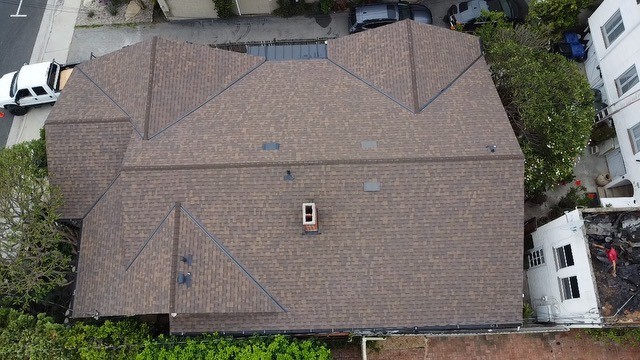Overhead view of a brown asphalt shingle roof with hips, valleys, a chimney and small roof vents