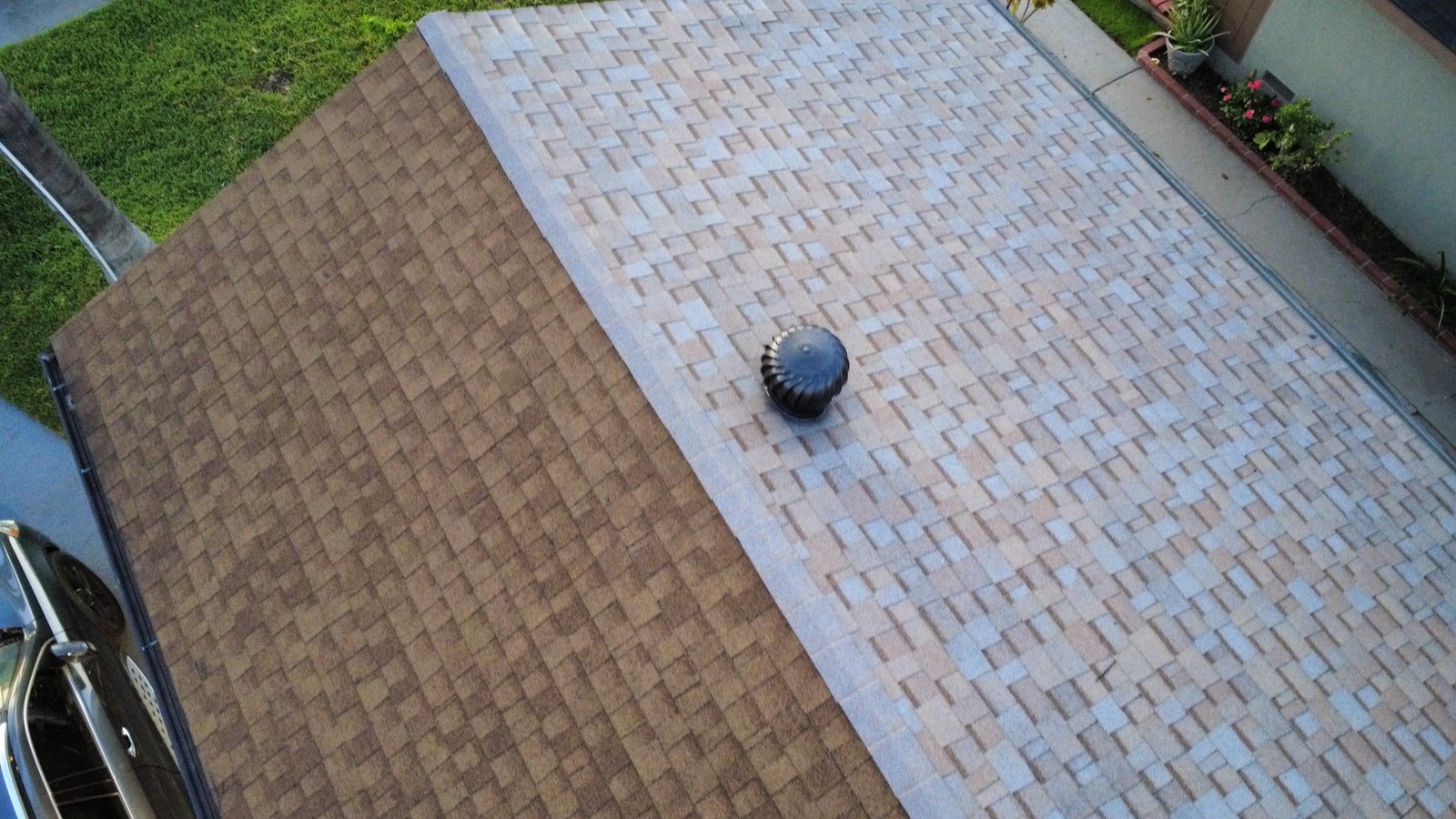 Aerial view of a two-tone asphalt shingle roof with a dark turbine vent near the ridge