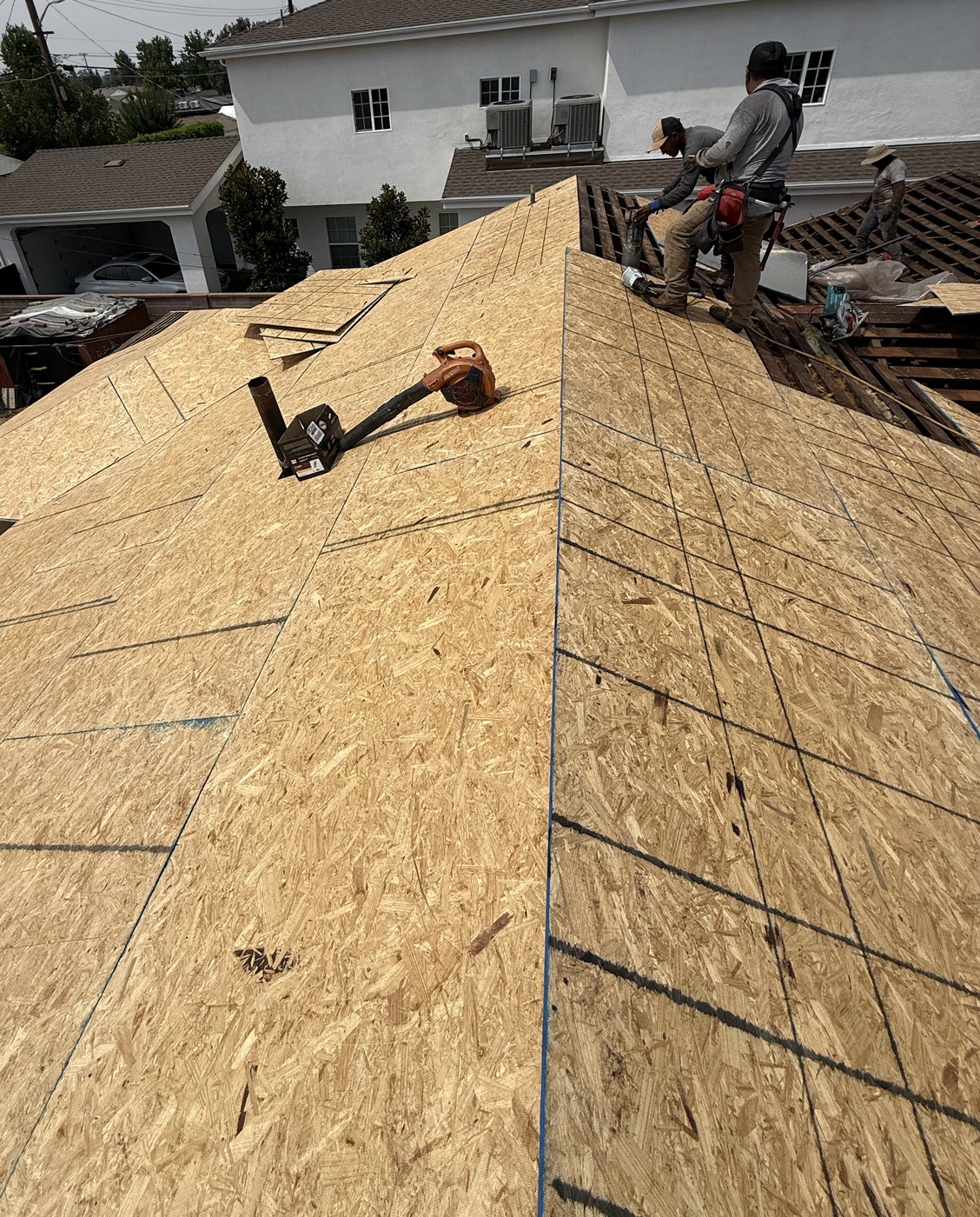 Workers on a bare OSB roof deck, with old spaced boards still exposed near the right edge.