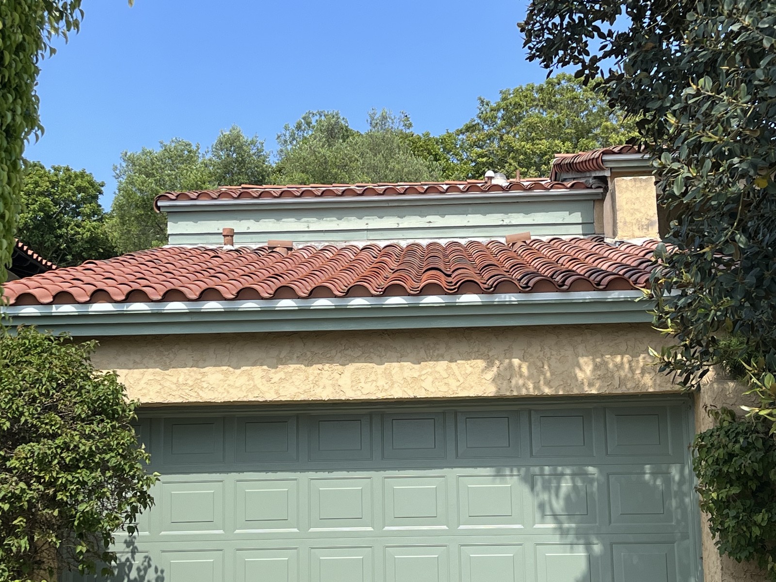 Red barrel tile roof above a garage with a sage green door and stucco wall