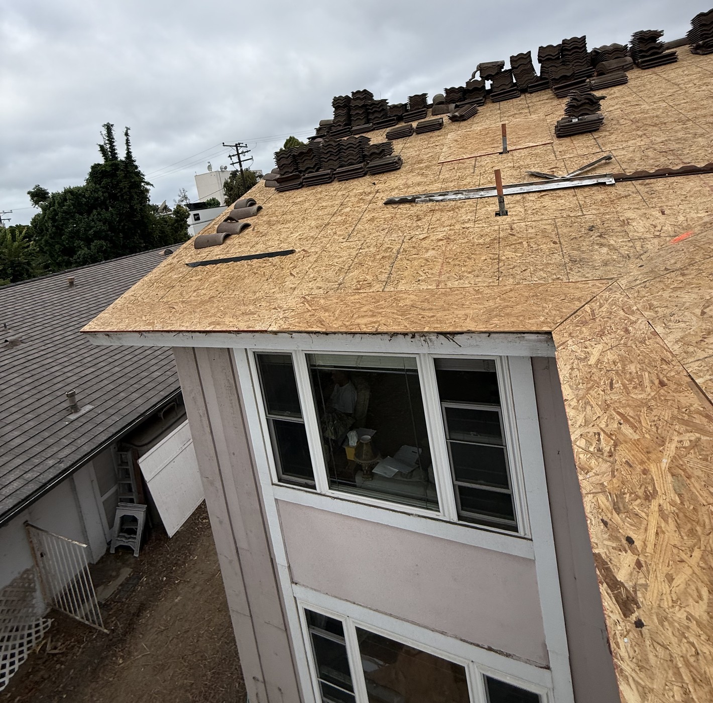 Stacks of brown roof tiles staged on new OSB sheathing above a home's bay window
