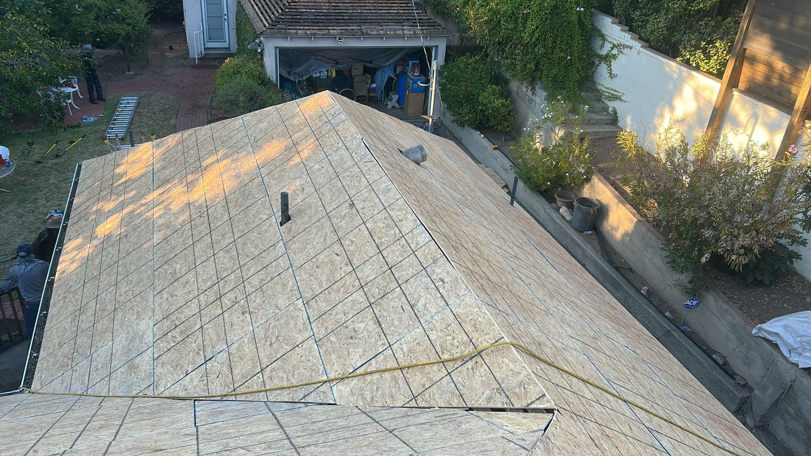 Exposed OSB roof deck marked with layout lines, two round vent pipes and a yellow hose across one slope.