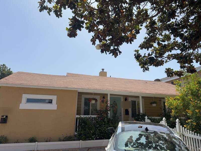 Single-story stucco house with a light shingle roof, white picket fence and a leafy tree overhead.